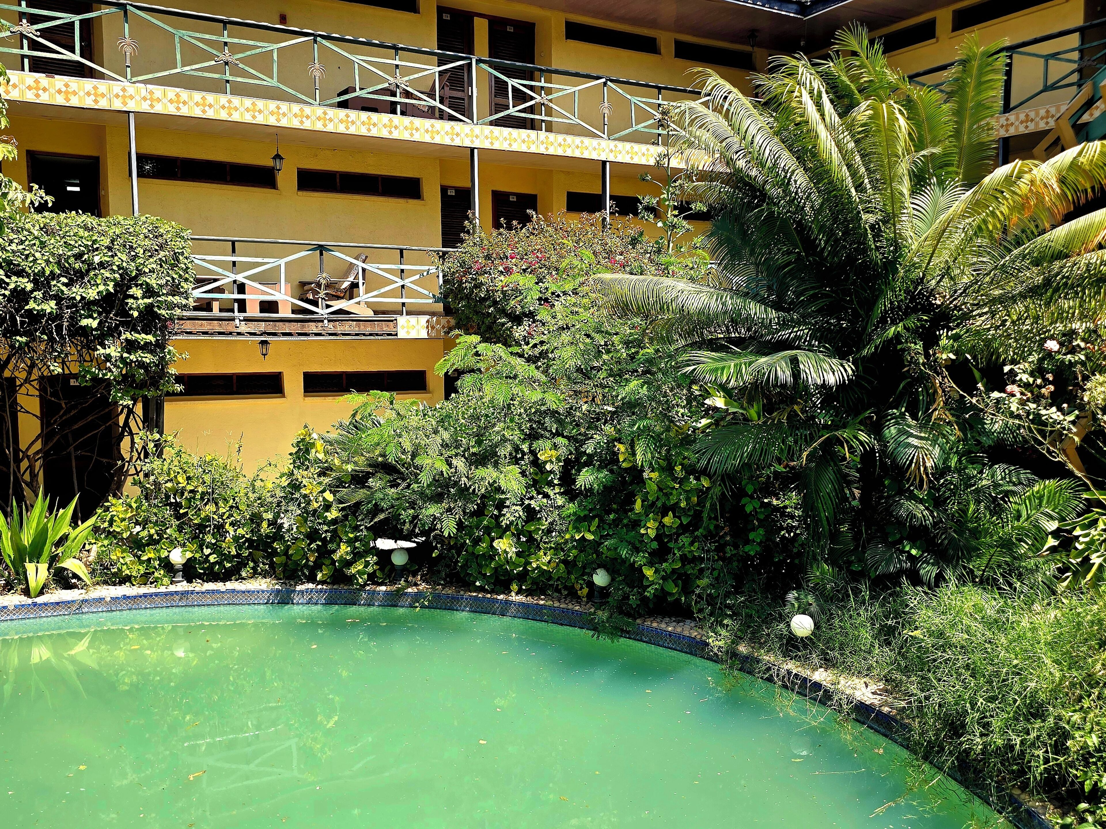 A pool surrounded by lush greenery and a yellow building with multiple windows and balconies.