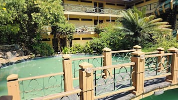 Un área de piscina con valla de madera, rodeada de abundante vegetación y un edificio de varios pisos con balcones.