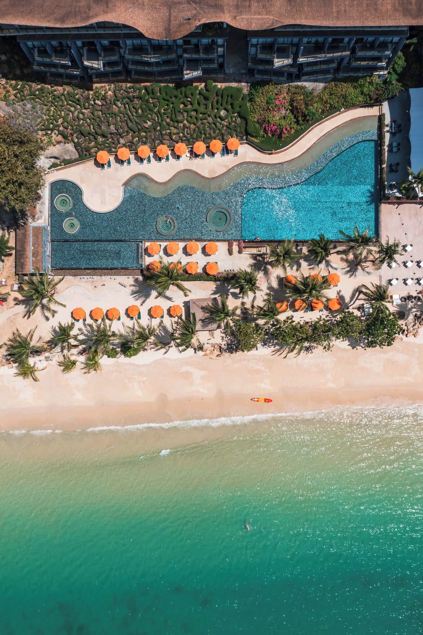 Vista aérea de un resort con una amplia piscina, numerosas tumbonas y una zona de playa.