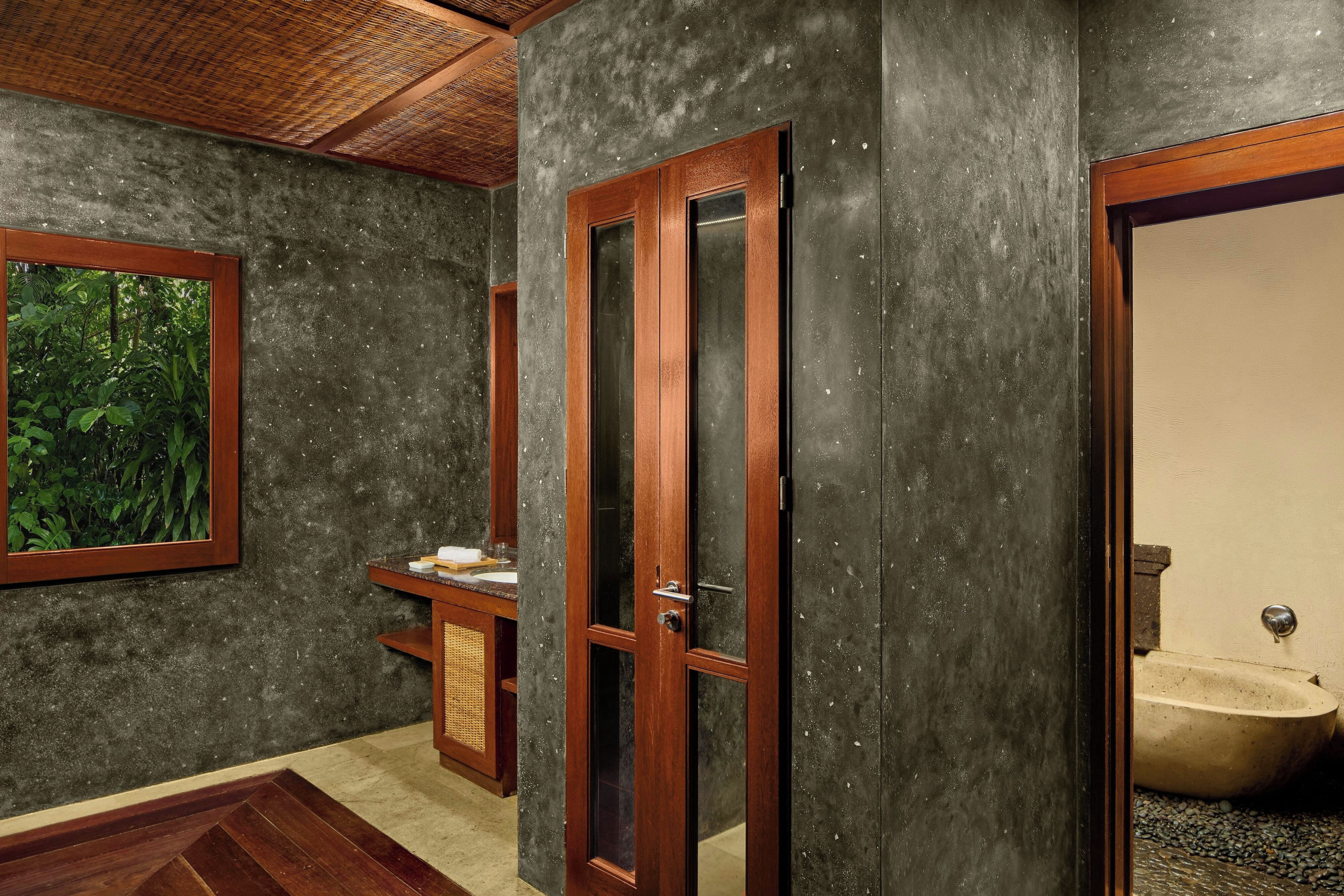 Baño con puerta de madera, lavamanos y ventana con vista a follaje.