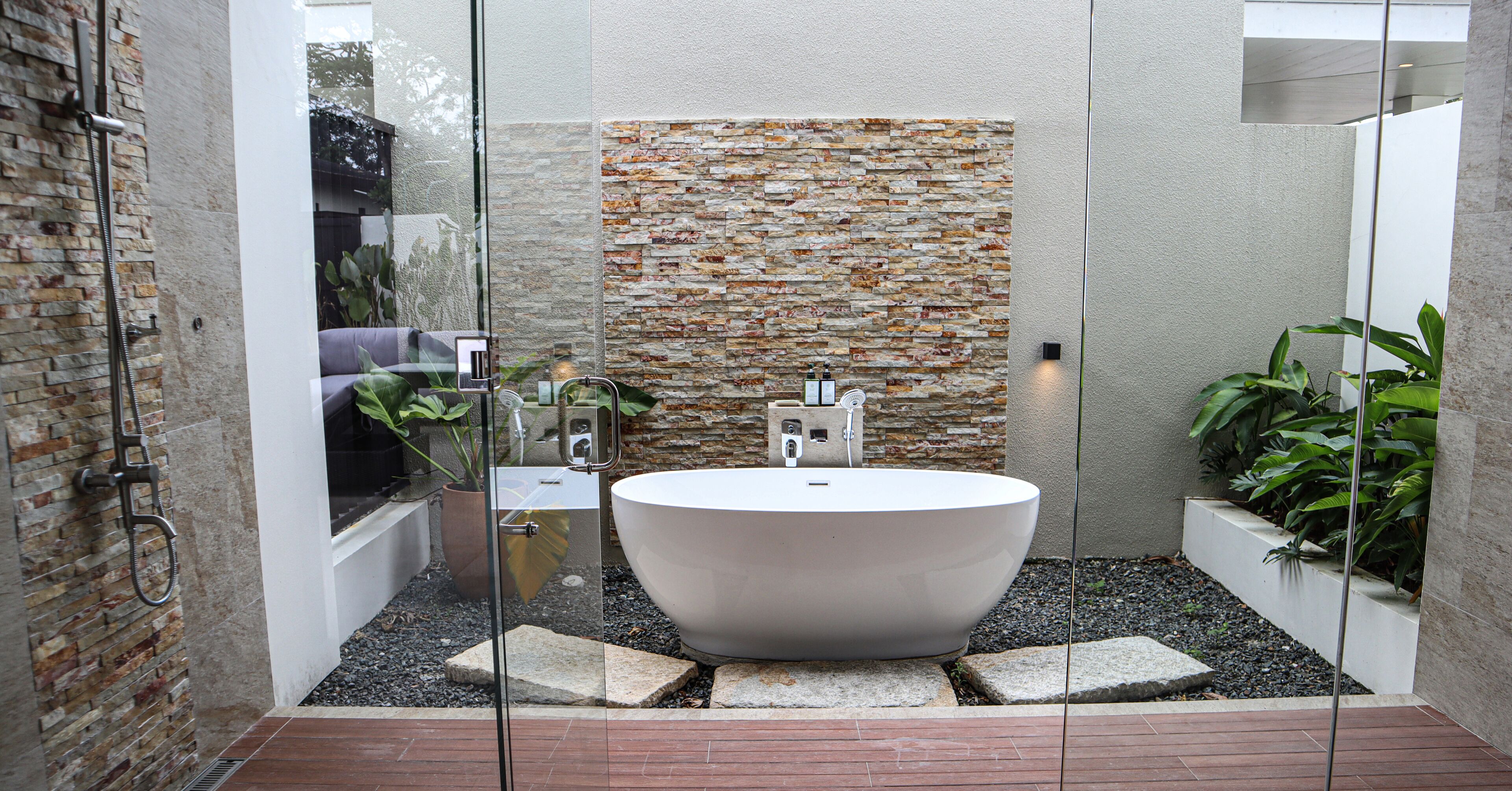 A modern bathroom with a freestanding bathtub, a glass shower enclosure, and a textured stone wall.
