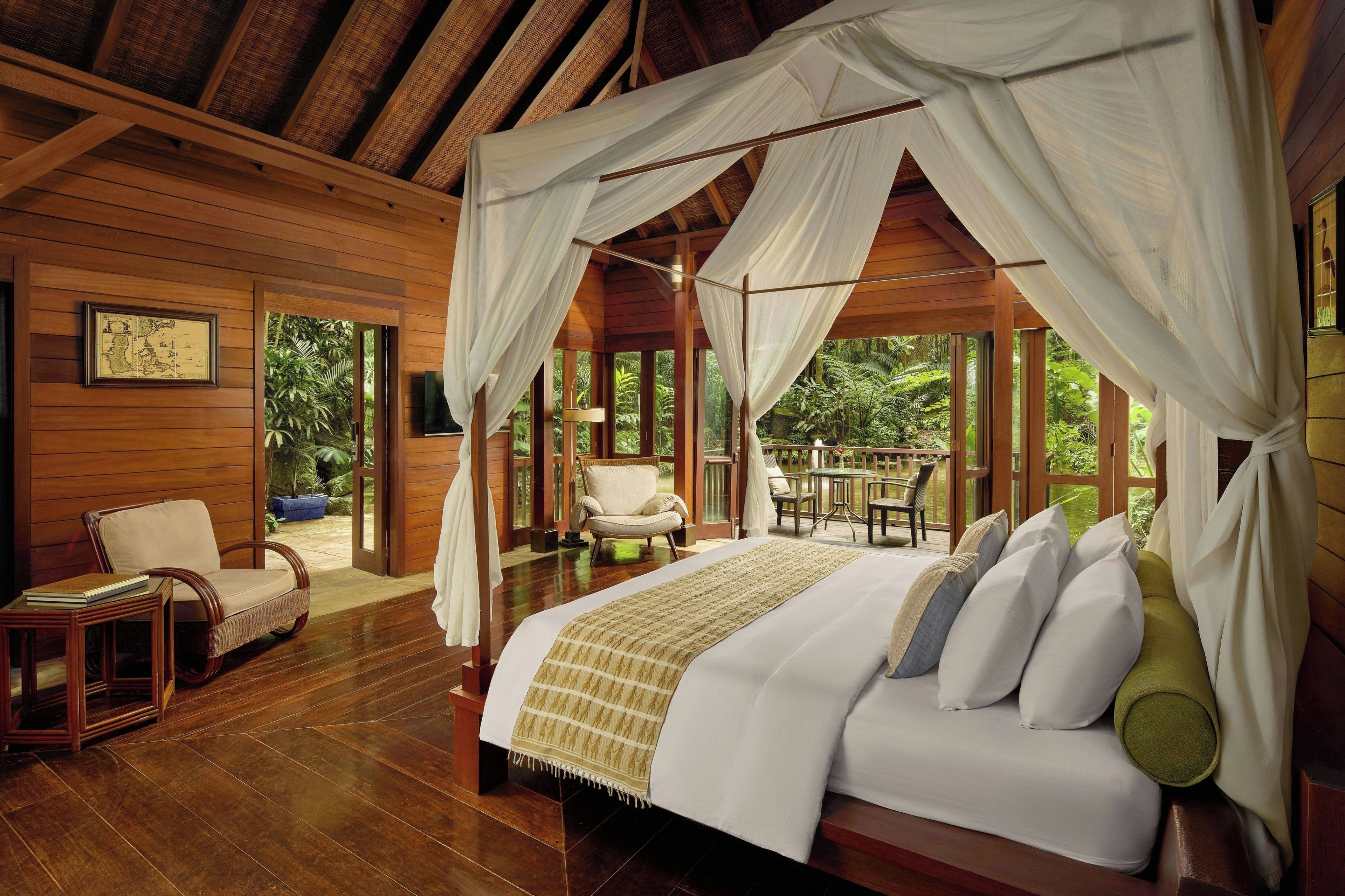 A spacious bedroom with a large bed, a sitting area with a chair and table, and a view of lush greenery outside.