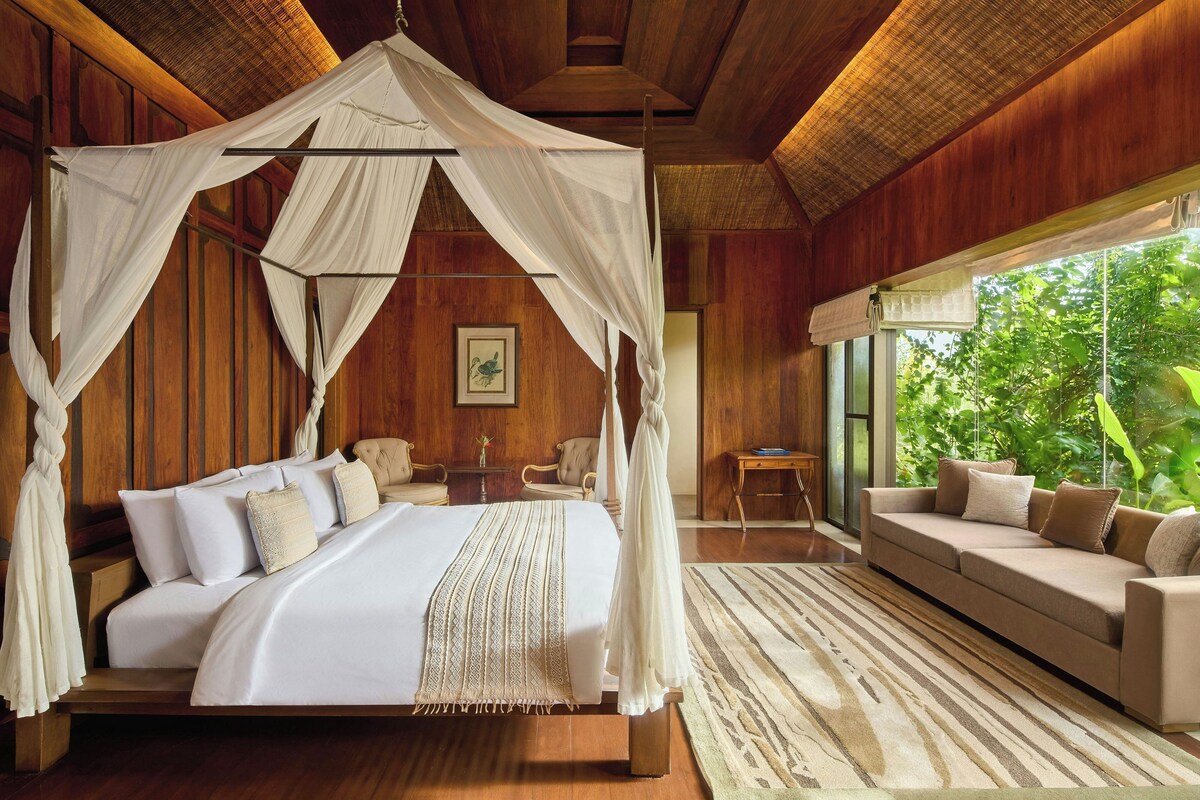 A spacious bedroom with a canopy bed, a sofa, and a view of lush greenery.