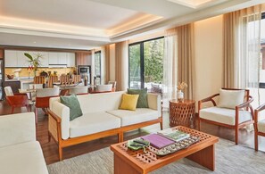 A modern living room with a sofa, chairs, a coffee table, and a kitchen in the background. - The Farm at San Benito, Autograph Collection (Lipa)
