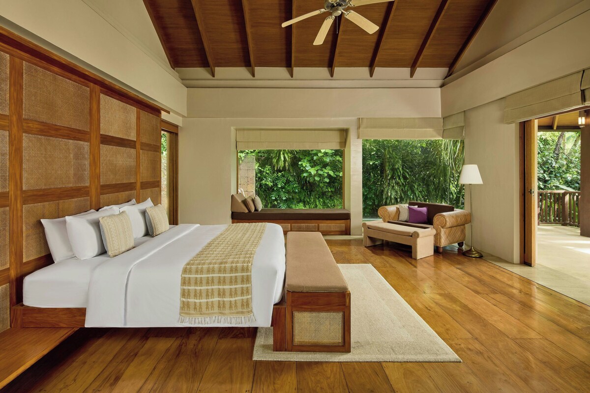 A bedroom with a large bed, a bench, a sofa, and a view of greenery outside.