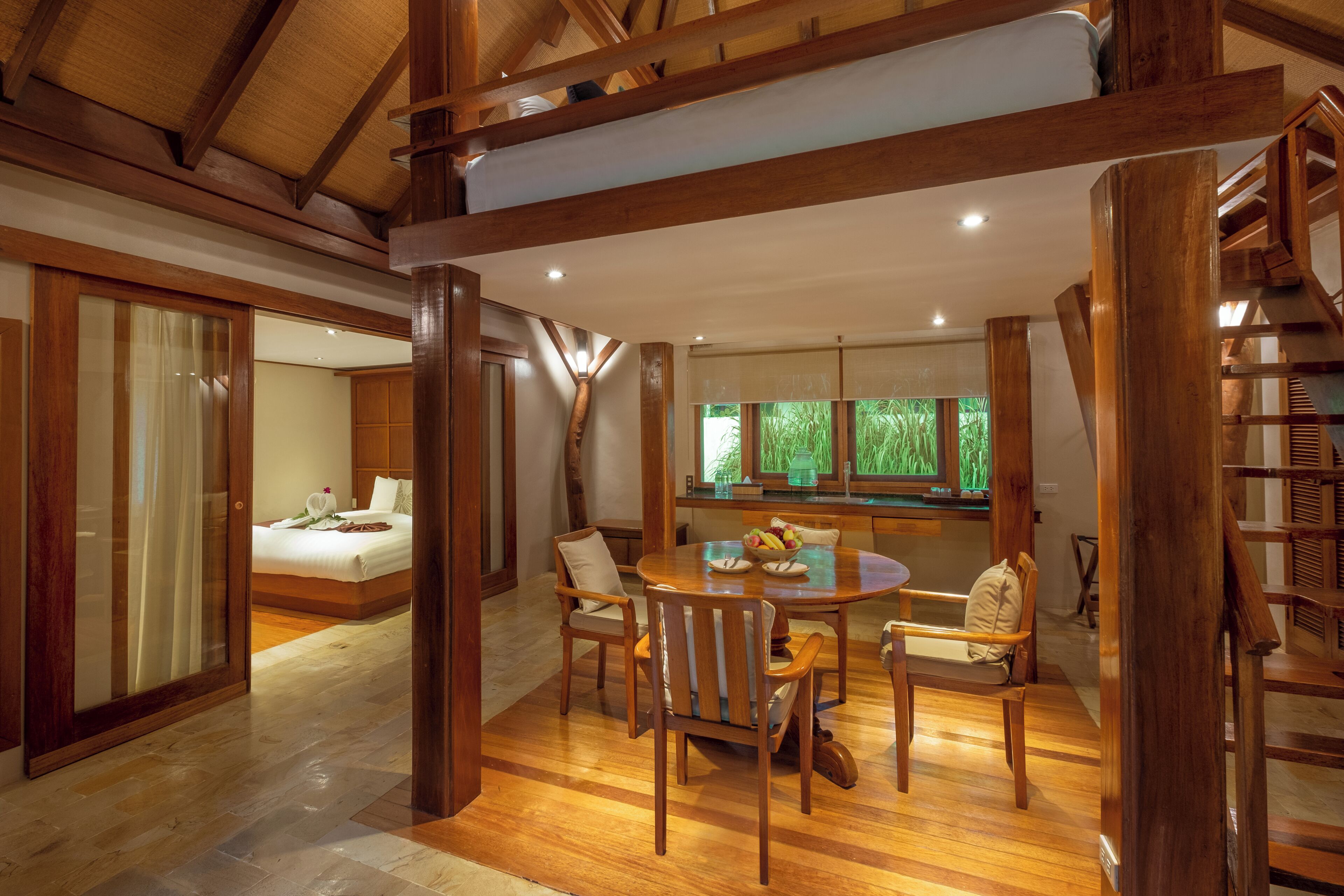 A spacious room with a wooden dining table, chairs, a bed, and a staircase.