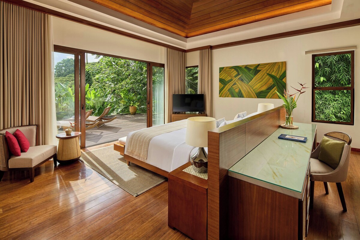 A modern hotel room with a large bed, a desk, a TV, and a view of the outdoors.
