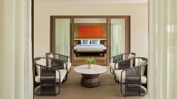 A hotel room with a bed, two wicker chairs, a round table, and a decorative plant.