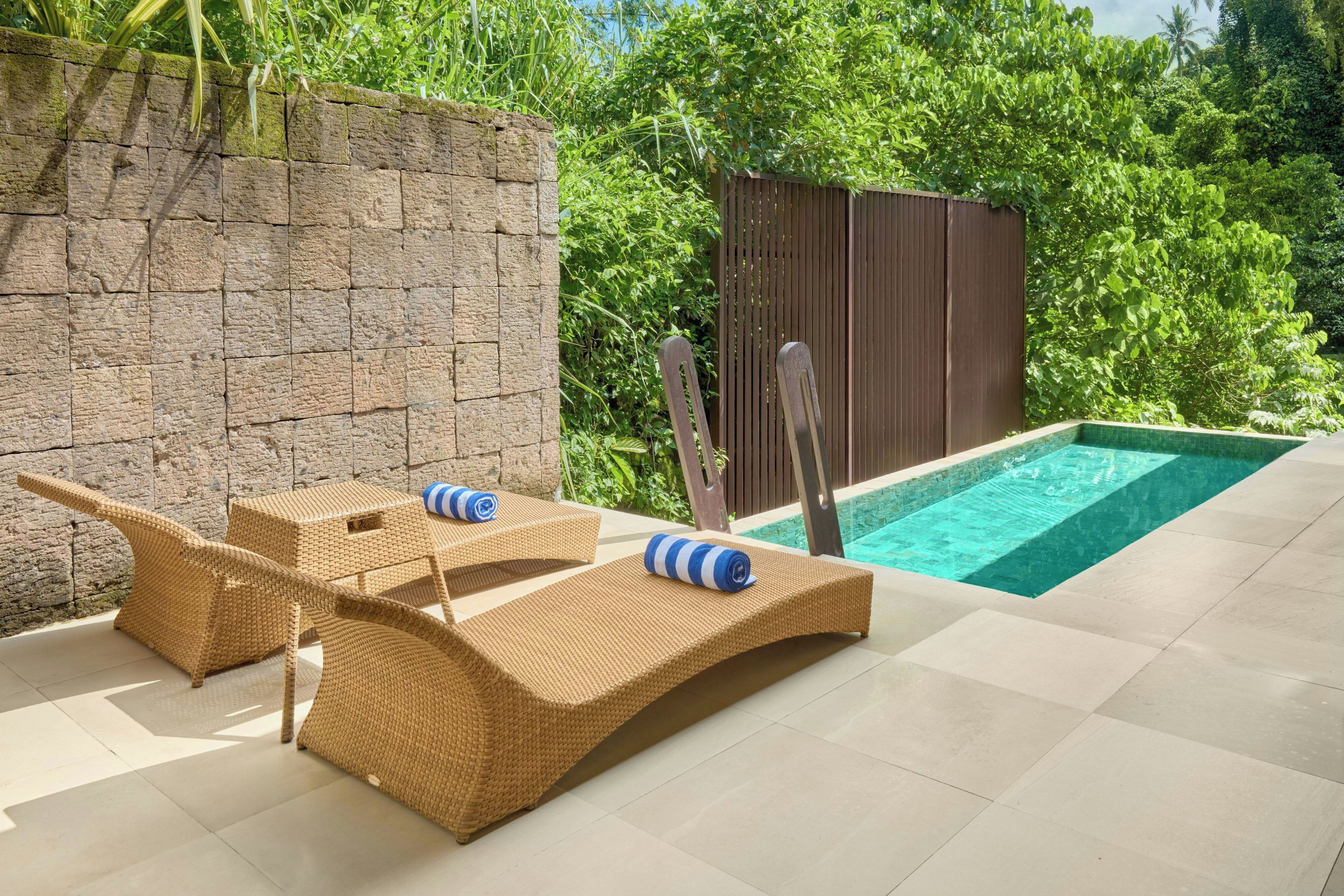 A poolside area with two lounge chairs, a wooden deck, and a stone wall.