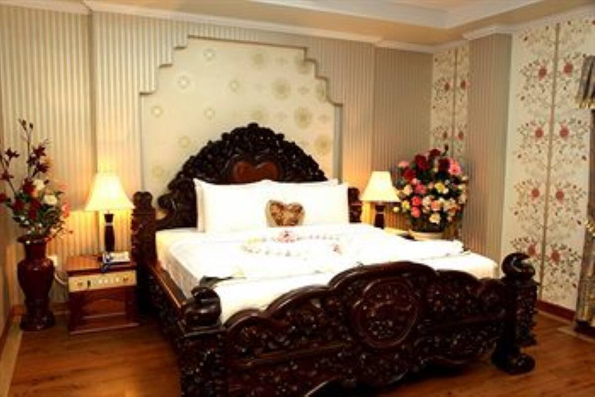 A classic four-poster bed with a floral headboard, bedside tables with lamps, and a floral-patterned wall.