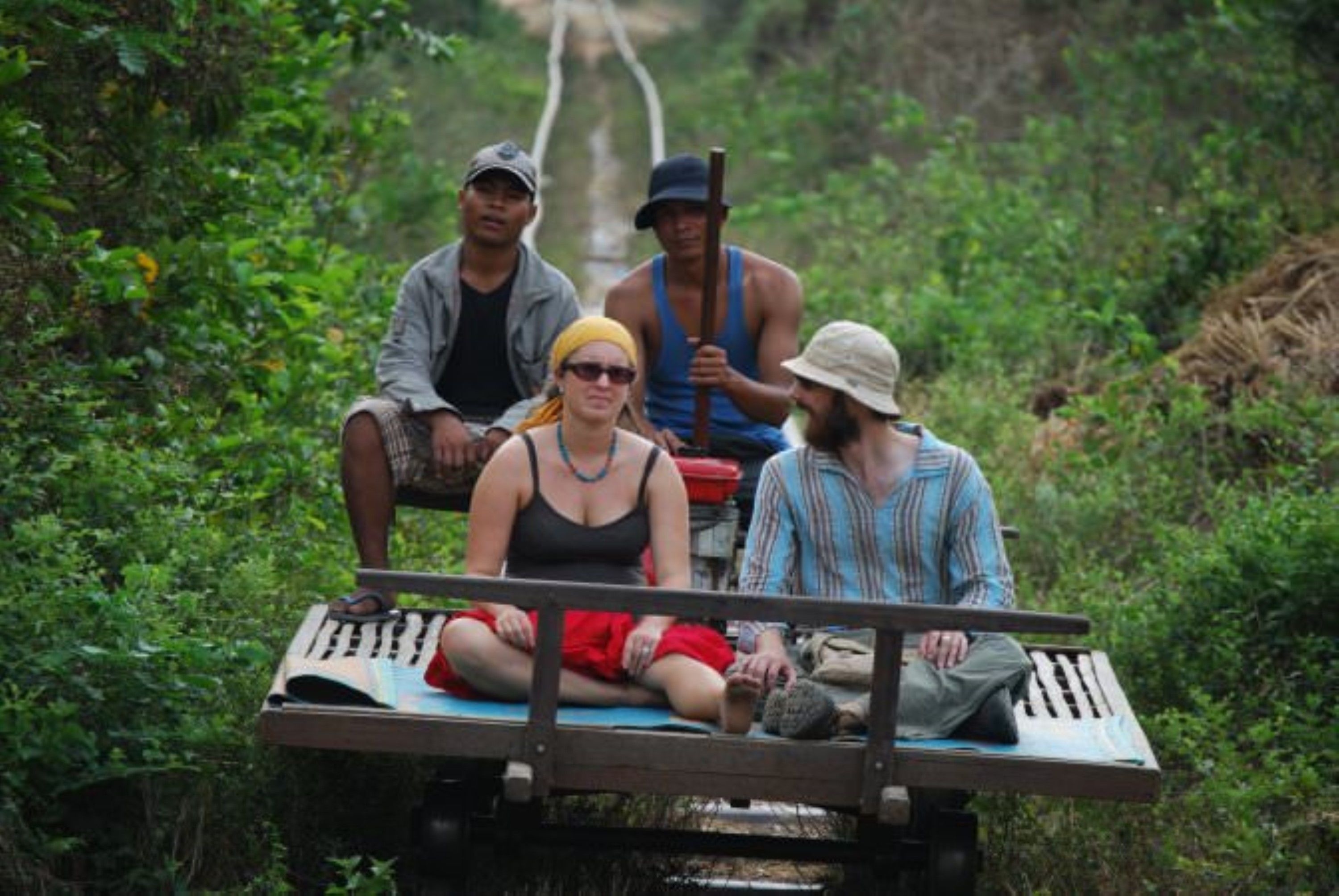 Four people on a wooden bench in a lush, green environment.