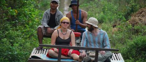 Four people on a wooden bench in a lush, green environment.