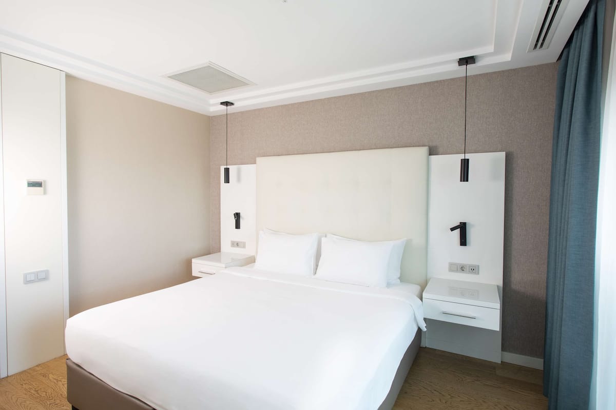 Ein Hotelzimmer mit einem großen Bett, einem Nachttisch, einem Kleiderschrank und einer wandmontierten Steuerung.