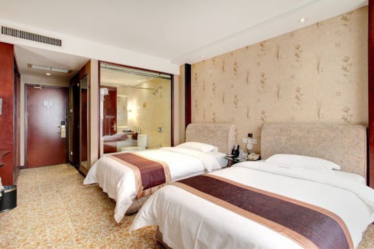 Ein Hotelzimmer mit zwei Betten, einem Badezimmer und einem Spiegel.