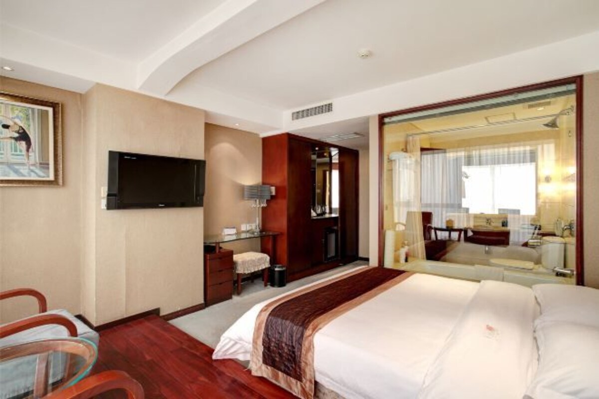 Ein Hotelzimmer mit einem großen Bett, einem Fernseher, einem Schreibtisch und einem durch eine offene Tür einsehbaren Badezimmer.