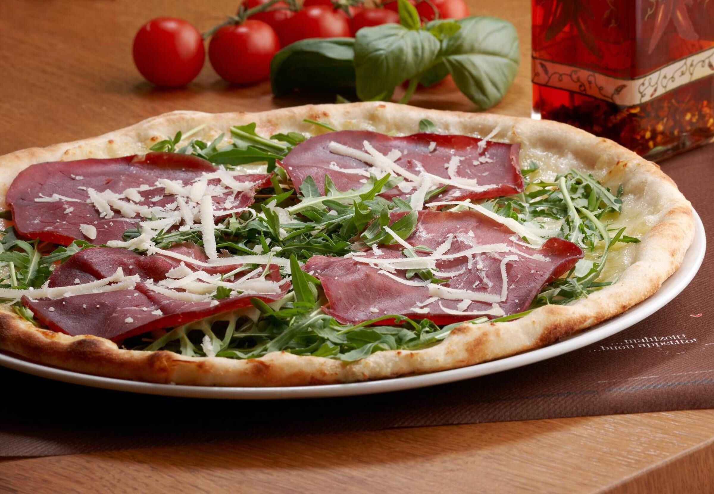 Pizza con rúcula y prosciutto sobre una mesa de madera.