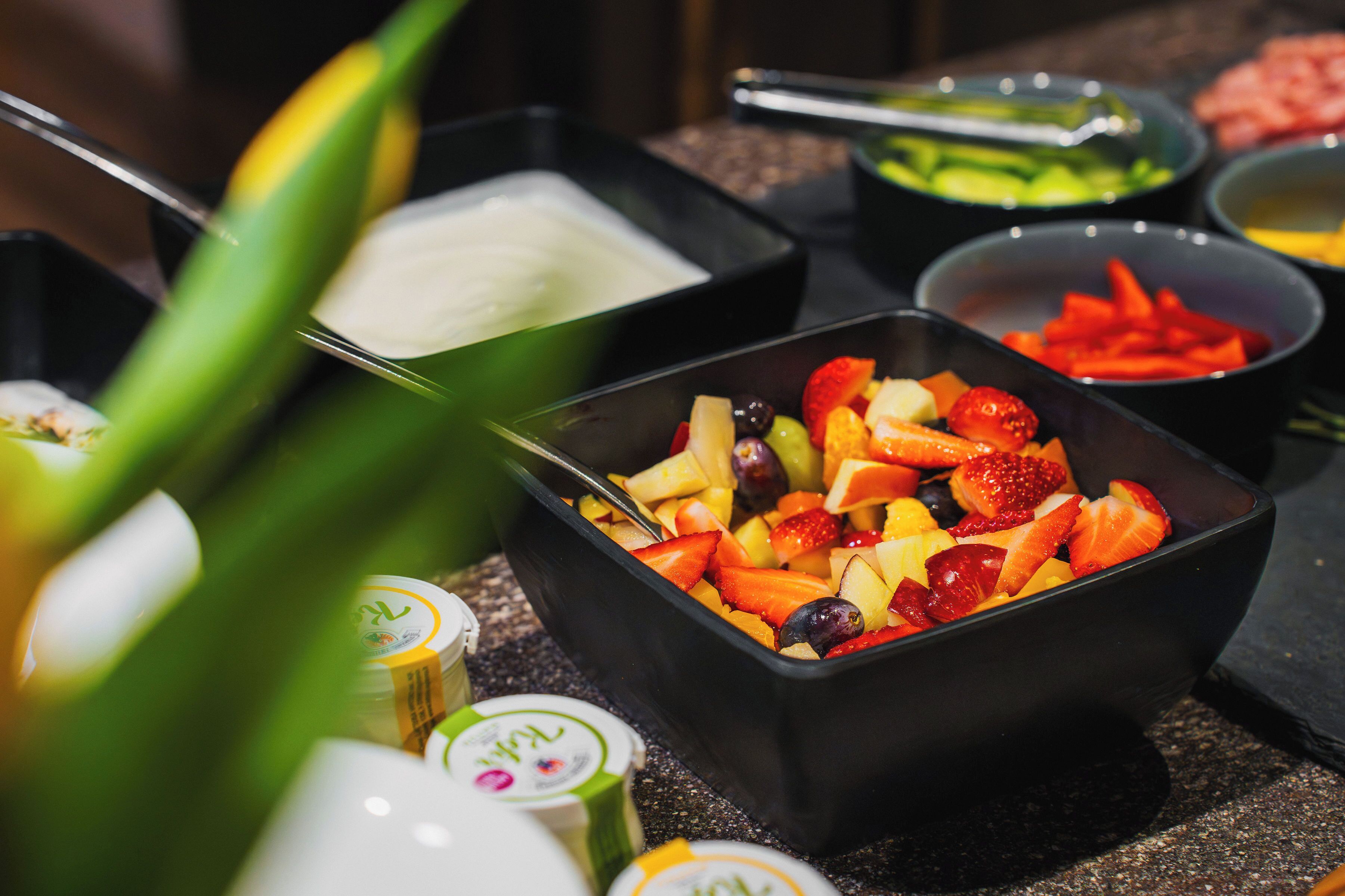 Une variété d’aliments, notamment des fruits et des yaourts, présentés dans des bols noirs et disposés sur une table.