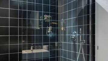 Une salle de bain moderne avec des carreaux noirs, une douche à l’italienne et un petit meuble-lavabo avec un miroir.