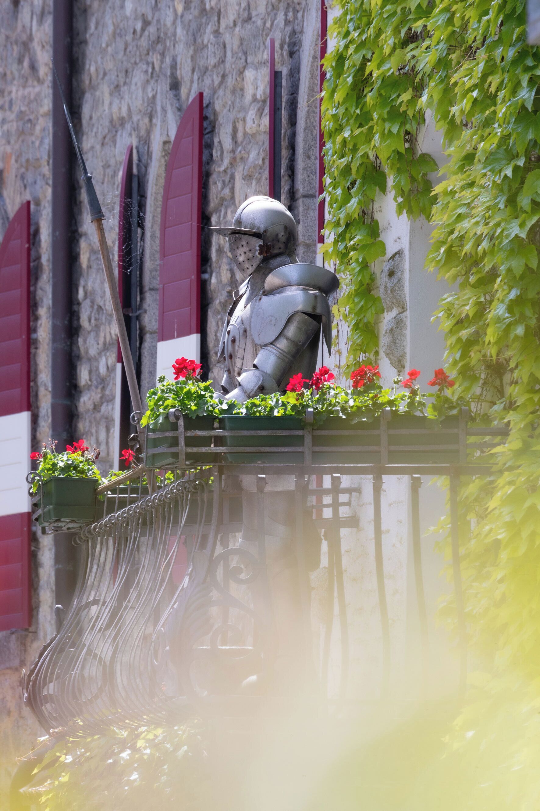 A statue of a knight in armor on a balcony with red flowers.