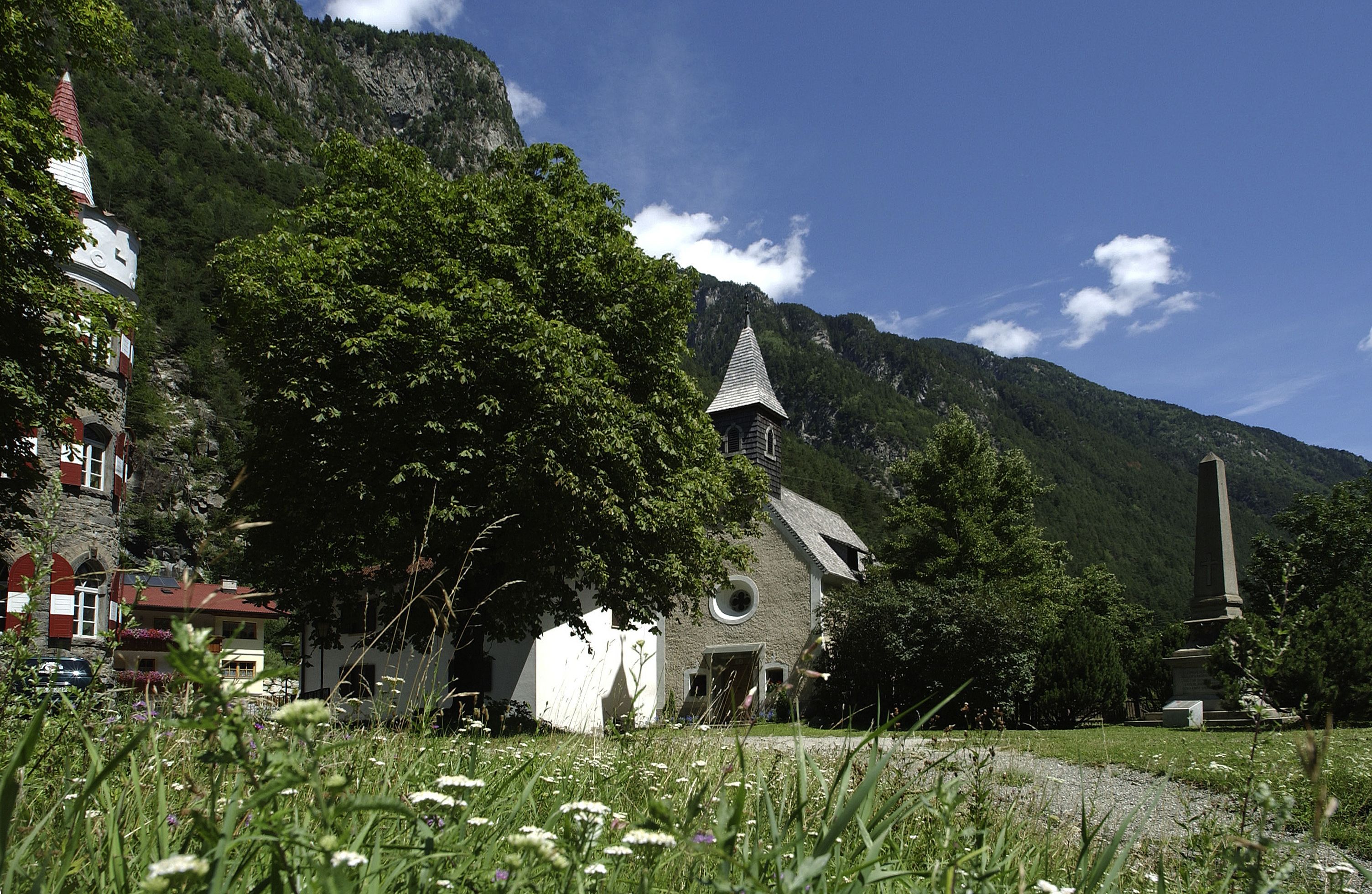 A church with a bell tower, surrounded by lush greenery and mountains.
