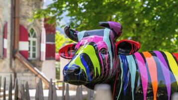 A colorful, striped animal sculpture near a building with a wooden fence and red and white windows.