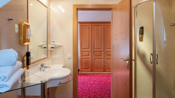 Baño con lavamanos de vidrio, un espejo, toallero y zona de ducha.