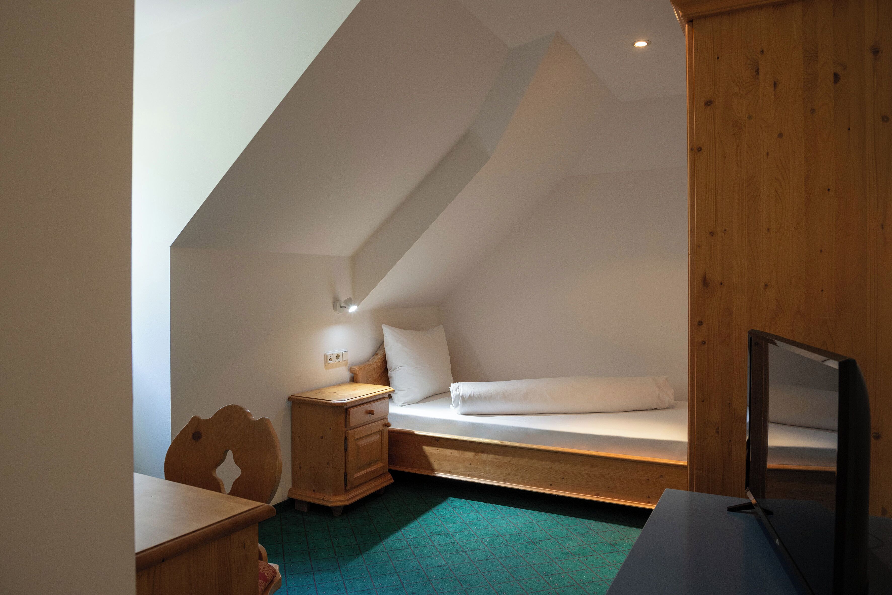 Una habitación pequeña y triangular con una cama, un escritorio y una silla.