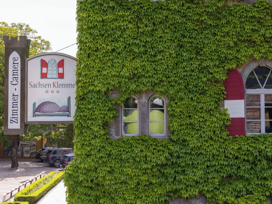 A building covered in green ivy with a sign for 'Sachsen Klemm' and a 'Zimmer - Kamera' sign.