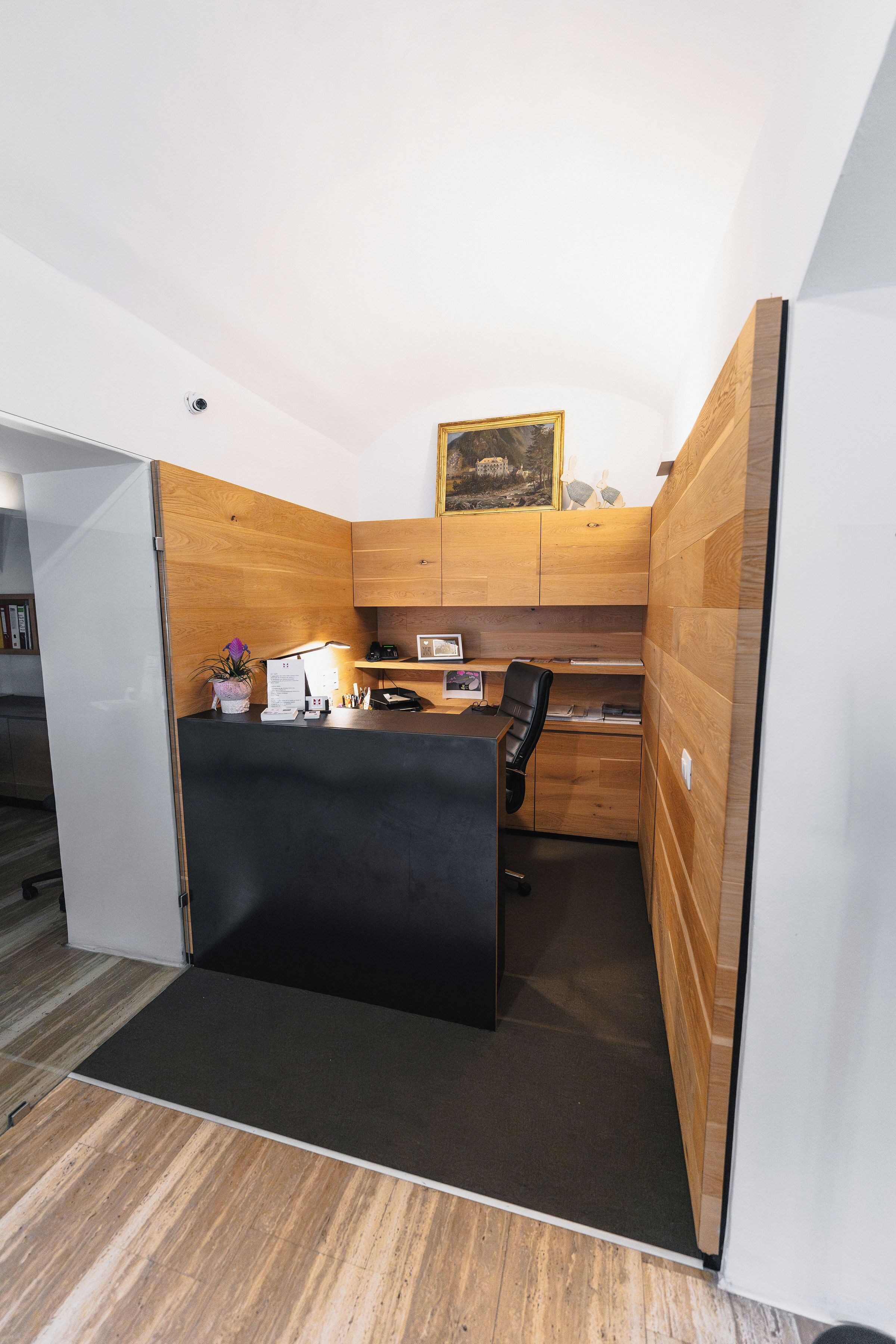 Ein moderner Arbeitsbereich mit Empfangstresen, Holzvertäfelung, einem schwarzen Bürostuhl und einem kleinen Schreibtisch mit einem Computer.