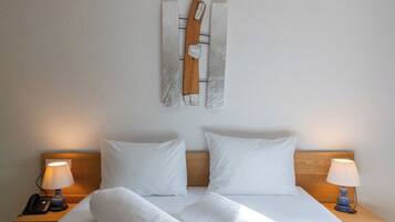 Una cama bien hecha con sábanas blancas, dos lámparas de noche y un cabecero de madera.
