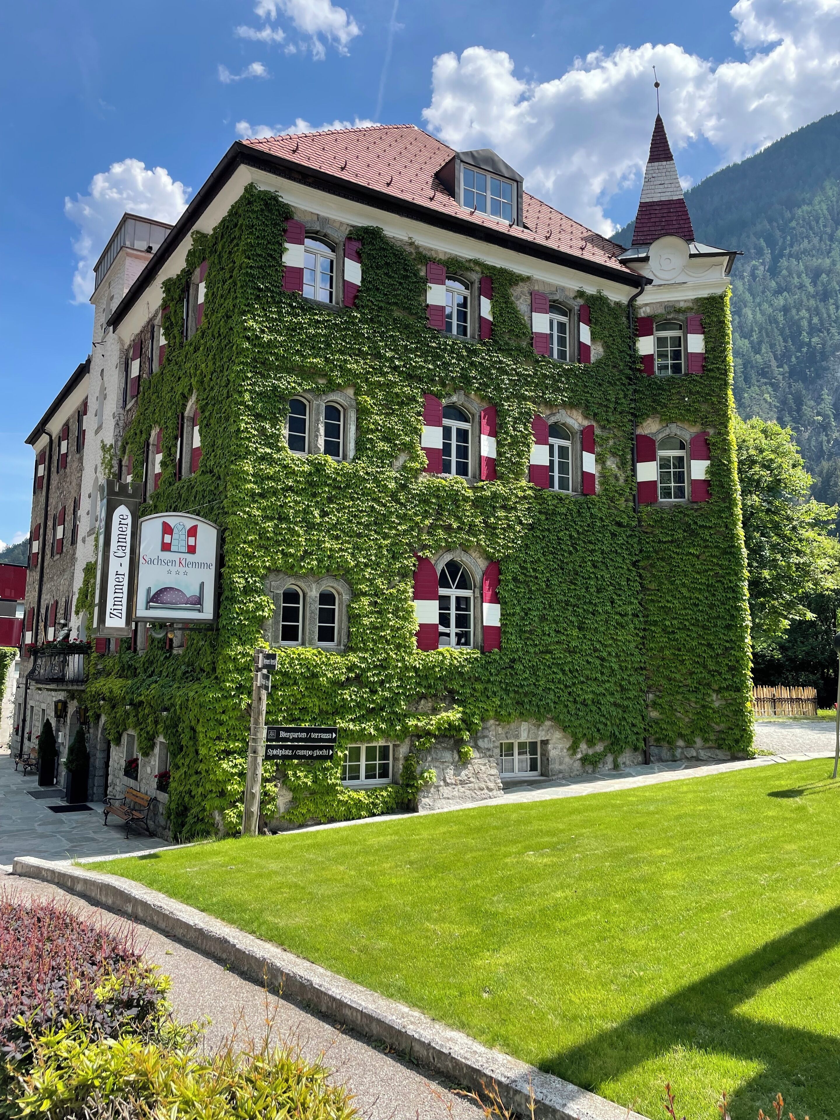 A historic building with ivy-covered walls, multiple windows with shutters, and a prominent tower.