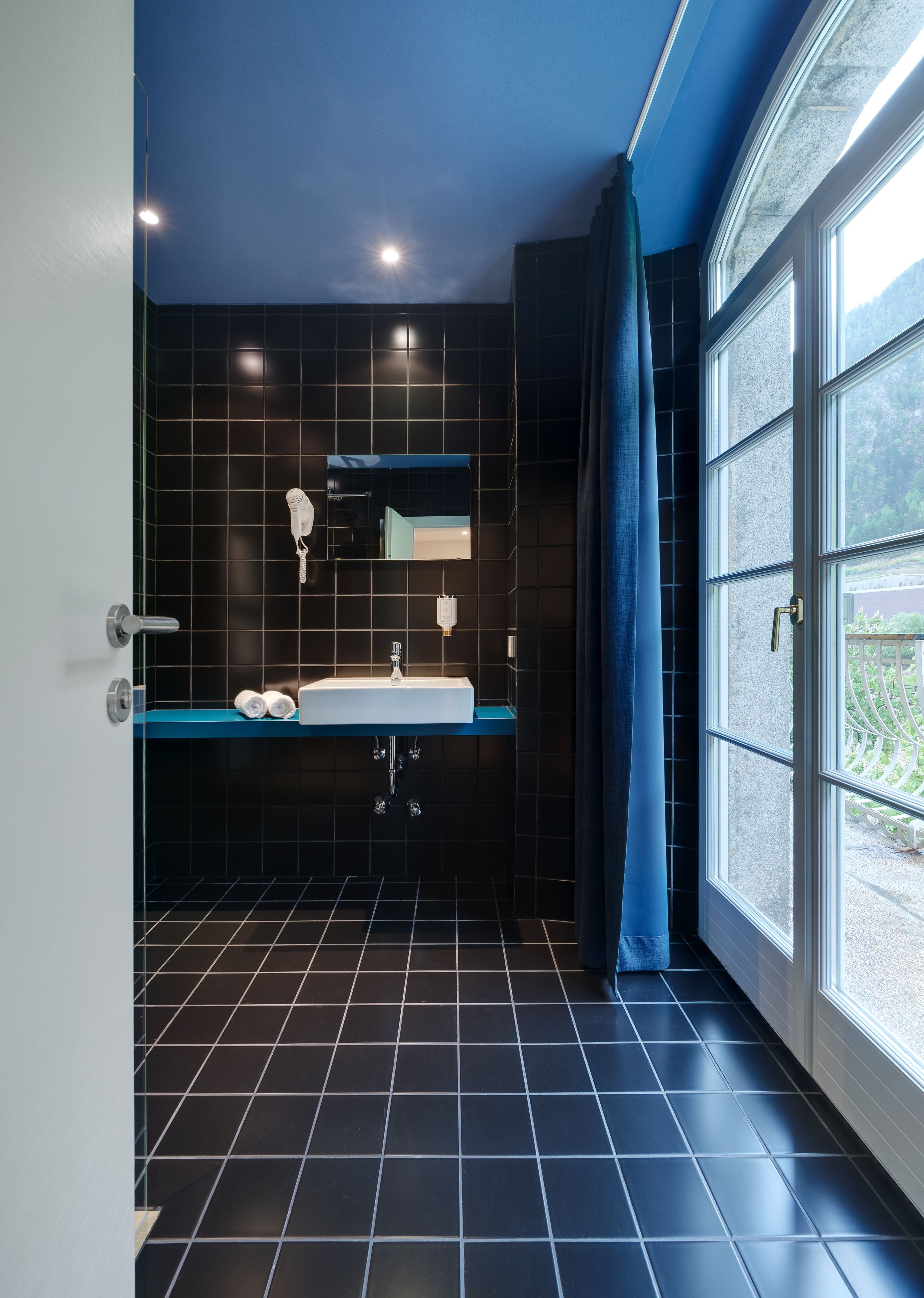 Een moderne badkamer met een zwarte betegelde vloer, een witte wastafel en een spiegel erboven.