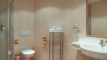 Un baño con cabina de ducha de vidrio, inodoro, toallero de vidrio con toallas, lavamanos y espejo.