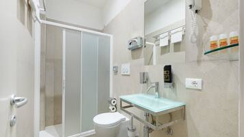A modern bathroom with a glass sink, a toilet, a shower, and a hairdryer on the wall.