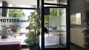 Entrada de hotel con puertas de vidrio, un mostrador de recepción y vistas al exterior.