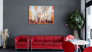 Un vestíbulo moderno con un sofá rojo, una mesa redonda y un cuadro abstracto grande en la pared.