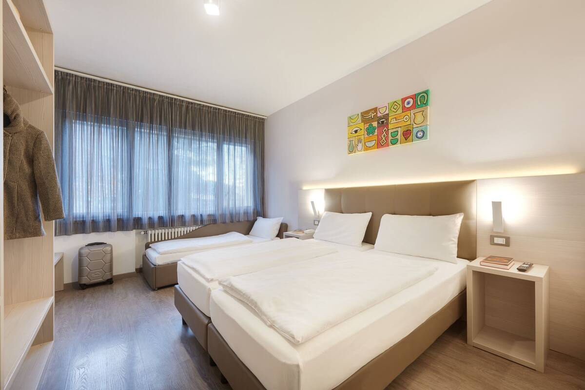 Habitación de hotel con dos camas, una maleta, un radiador y una pared con iconos de colores.
