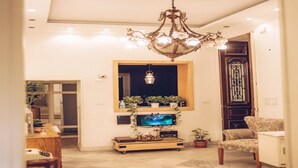 A living room with a chandelier, a television on a stand, a wooden cabinet, and a floral sofa. - Paris Hotel (Cairo)