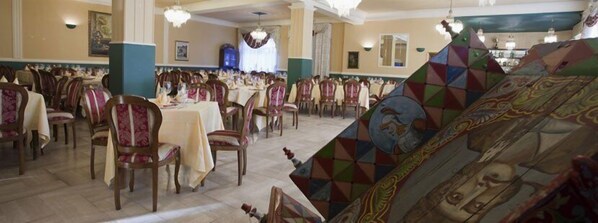 A banquet hall with multiple tables and chairs, a chandelier, and a large, colorful mural on the wall. - Hotel Scrivano (Randazzo)