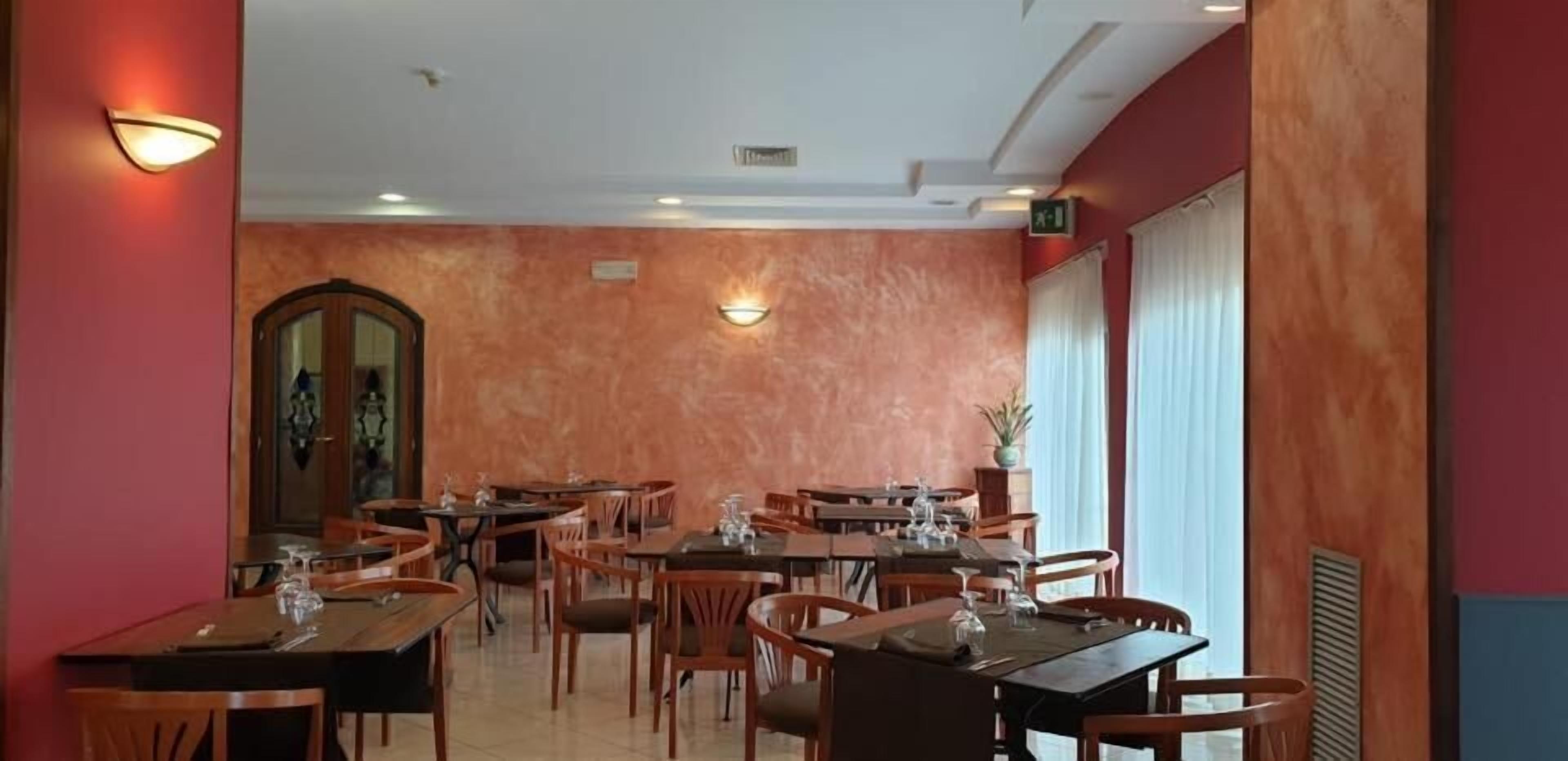 Een restaurant met meerdere tafels en stoelen, een grote spiegel en wandlampen.