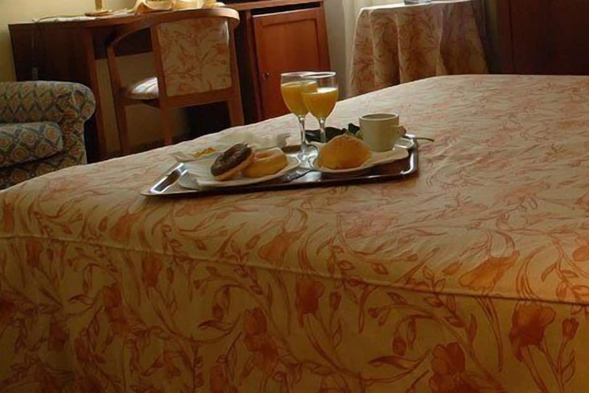 Una habitación de hotel con colcha de estampado floral, una bandeja con opciones de desayuno, como croissants y zumo de naranja, y una lámpara de mesa.