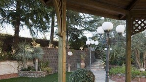 Ein überdachter Außenbereich mit einer Steinwand, Topfpflanzen und einer Holz-Pergola mit hängenden Lampen.