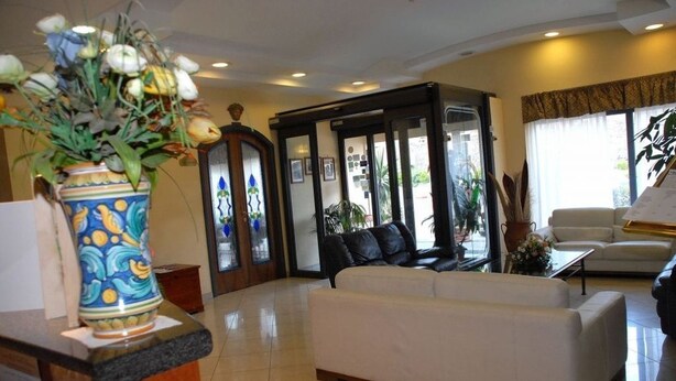 Eine moderne Lobby mit einem weißen Sofa, einer dekorativen Vase und einem Glastür-Eingang.