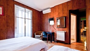 A hotel room with wooden walls, a bed, a desk with a chair, and a radiator. - Hostal Asuncion (Madrid)