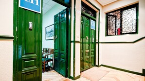 A hallway with green doors marked "CH" and a window with decorative iron bars. - Hostal Asuncion (Madrid)