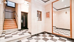 A hotel lobby with a checkered floor, a wooden staircase, a large mirror, and a door with a frosted glass panel. - Hostal Asuncion (Madrid)