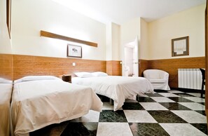 A hotel room with two beds, a white armchair, a wooden headboard, a checkered floor, and a framed picture on the wall. - Hostal Asuncion (Madrid)