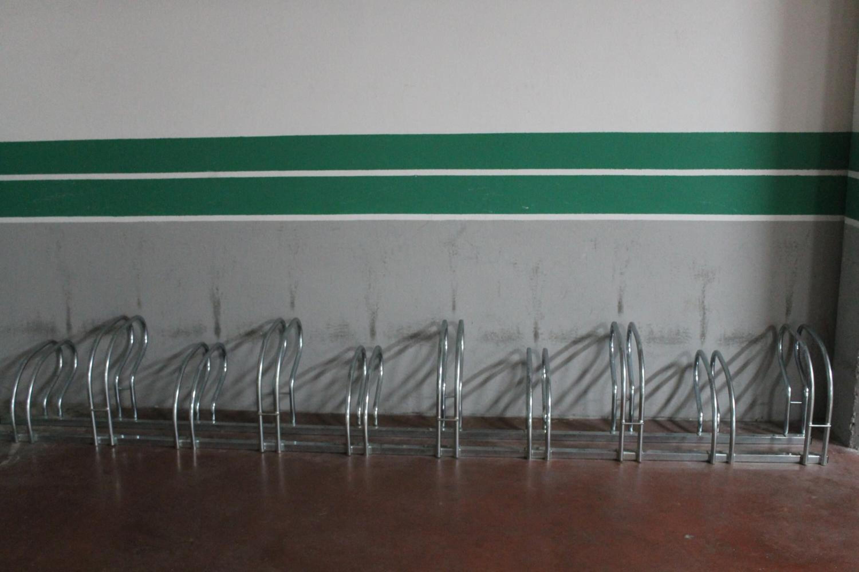 A metal rack with multiple hooks against a wall with a green stripe.
