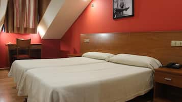 Habitación de hotel con dos camas, un escritorio, una silla y un cuadro en la pared.