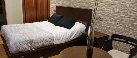 A bedroom with a bed, a round table, a chair, and a tall floor lamp.